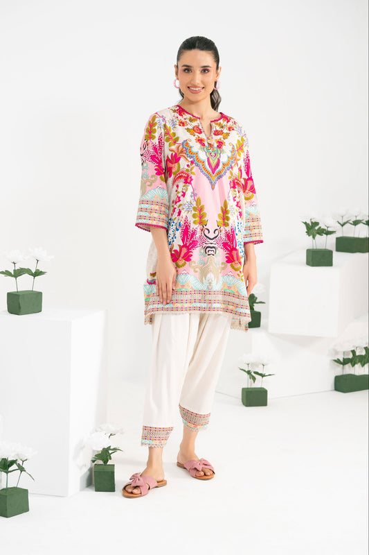 Woman wearing a colorful floral top and white pants standing in a minimalistic room with plants.