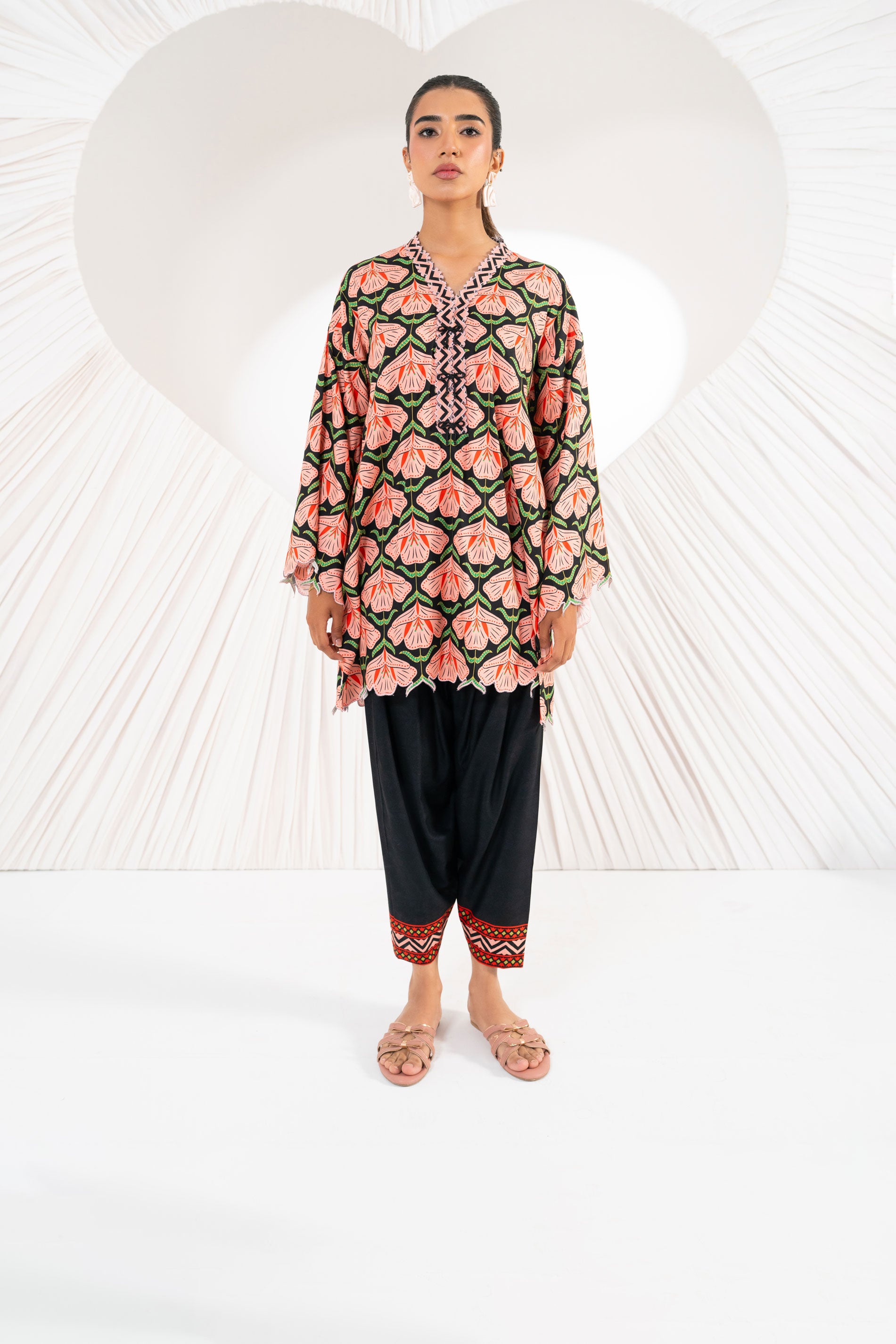 Woman wearing a floral patterned top and black pants against a white background