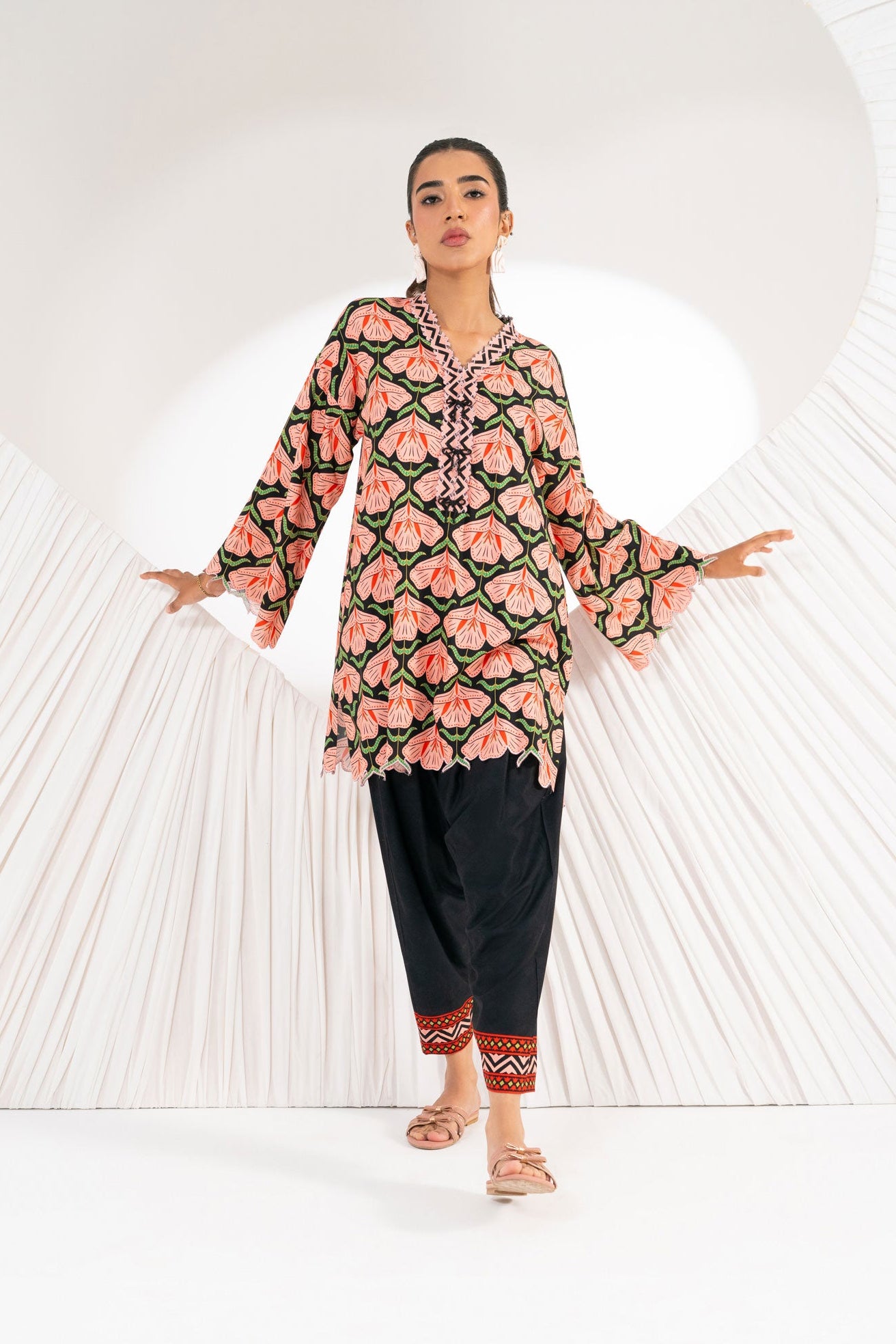 Woman wearing a floral patterned outfit with black pants against a white background