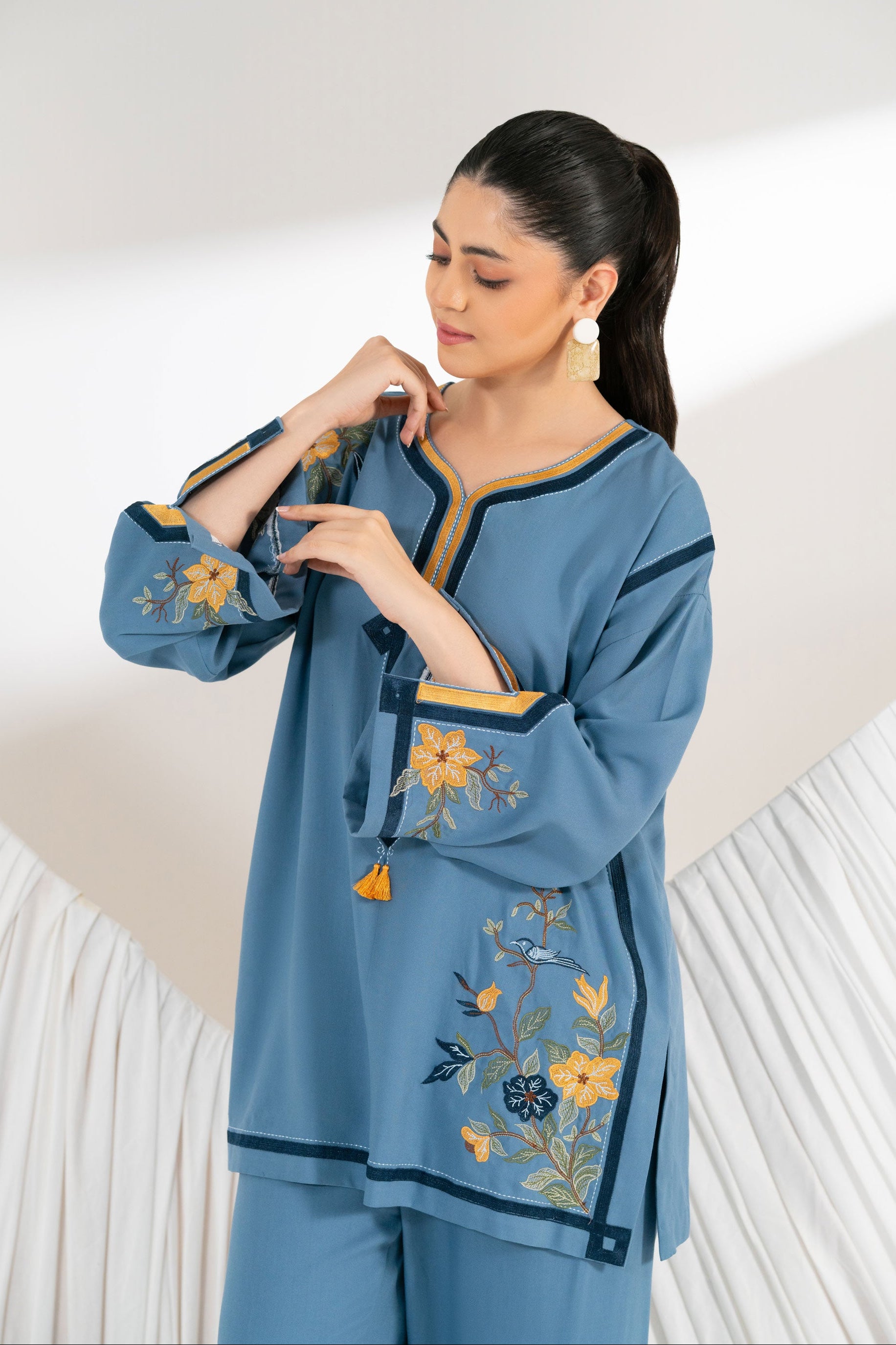 Woman wearing a blue embroidered outfit against a white background