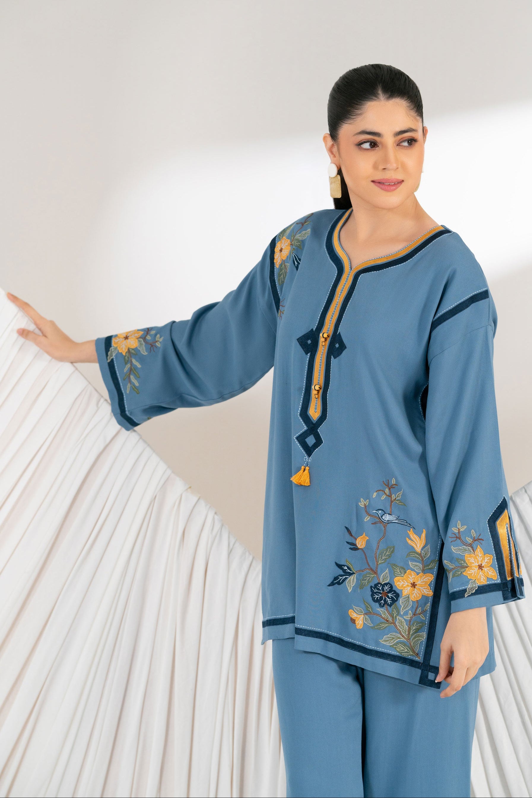 Woman wearing a blue embroidered outfit against a white background
