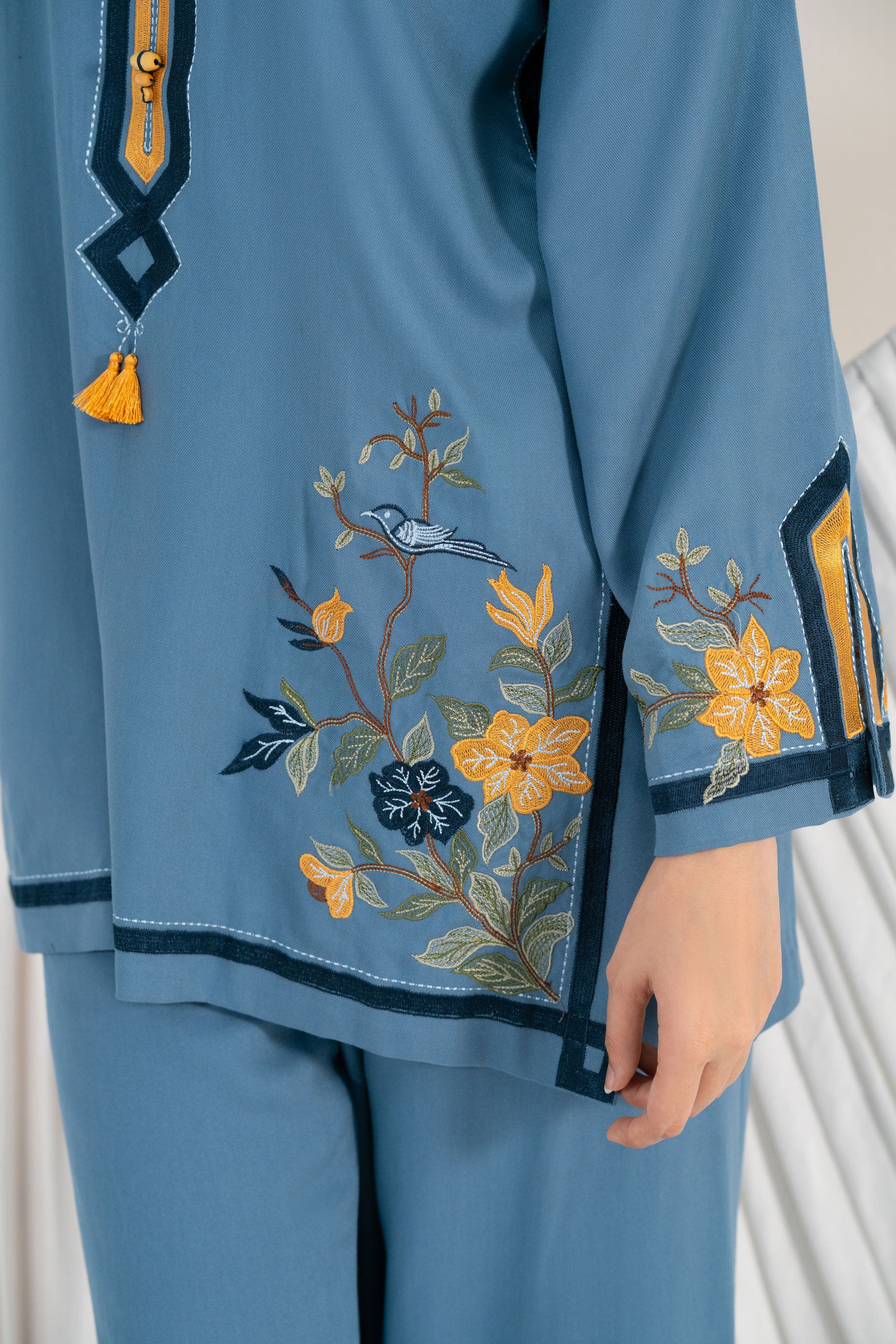 Blue embroidered outfit with floral and bird designs on a white background