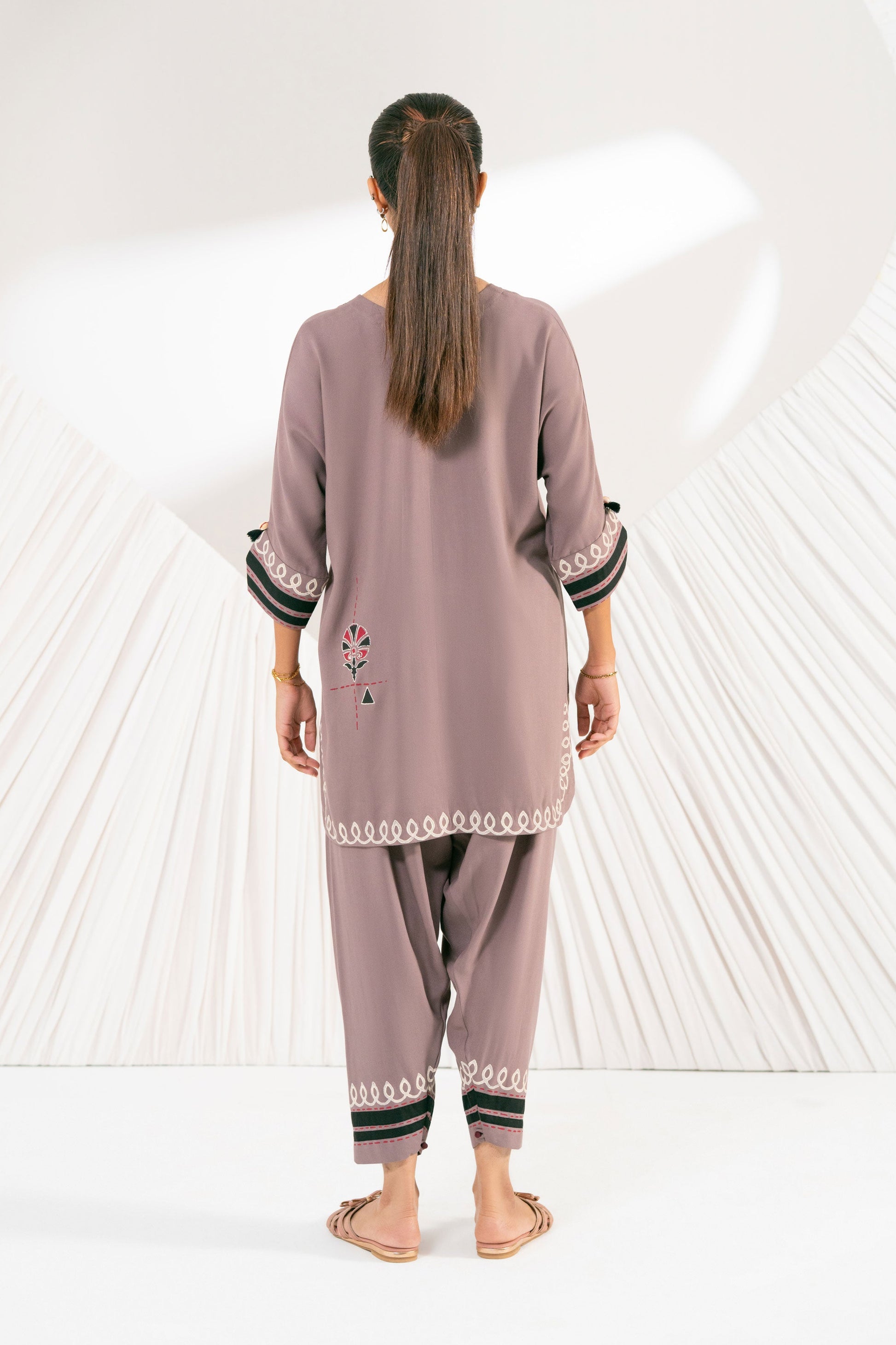 Woman wearing a mauve outfit with black trim against a white background