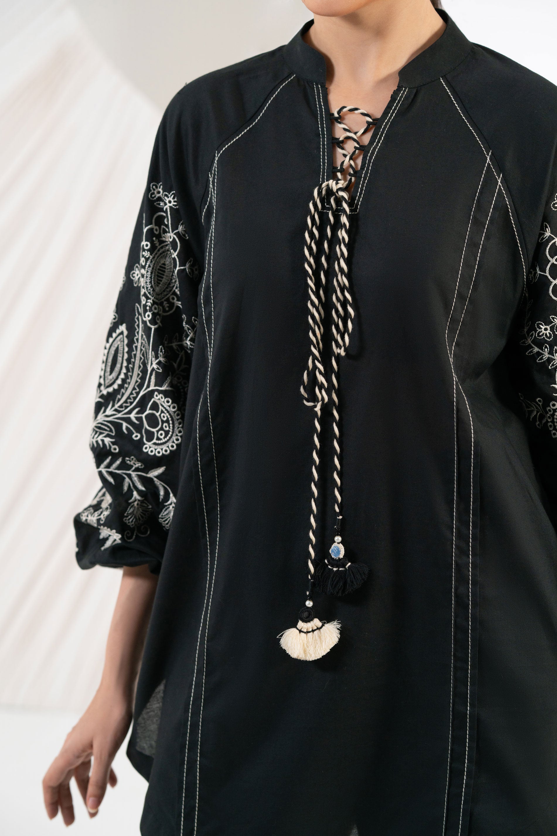 Person wearing a black outfit with intricate patterns and a long necklace.