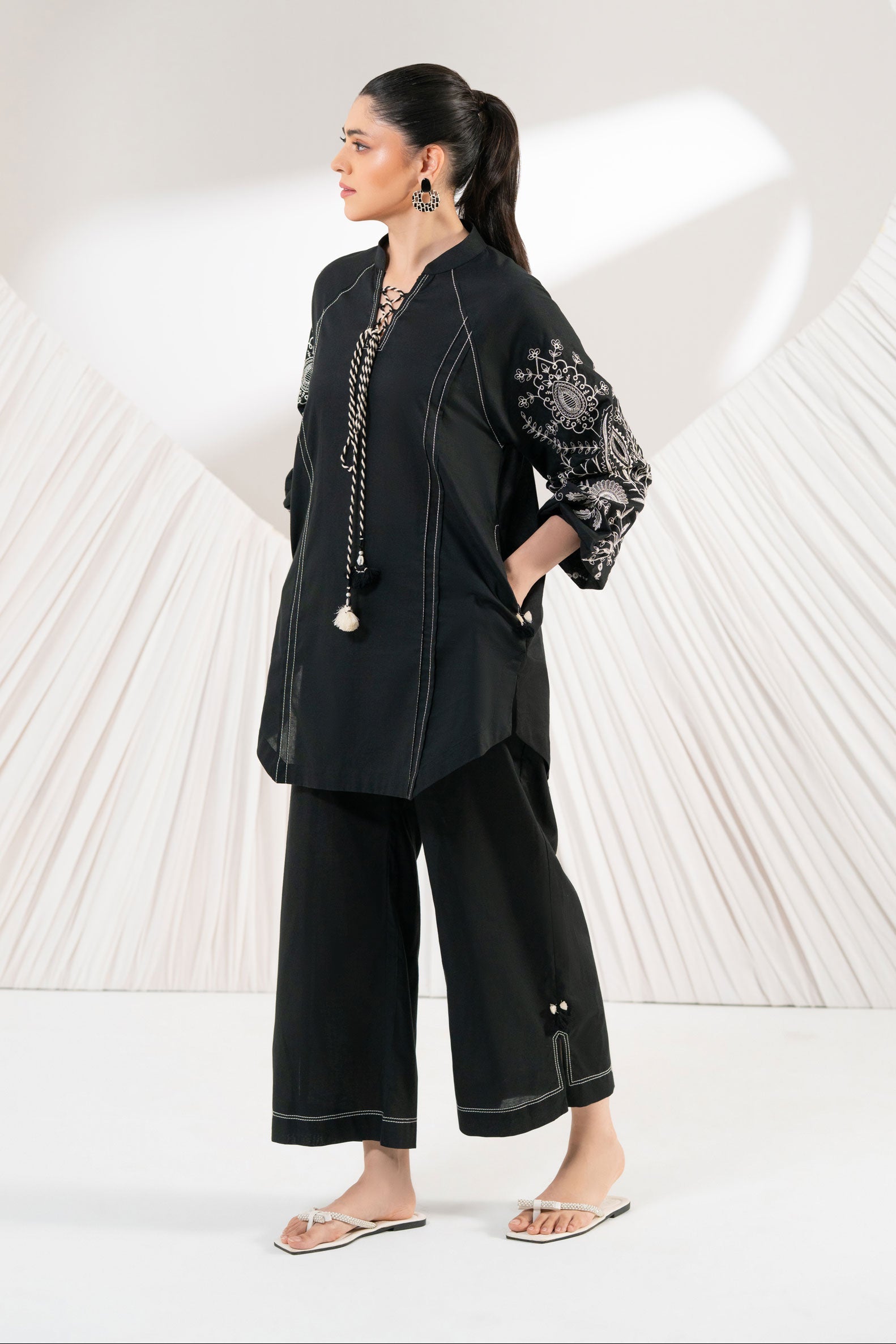 Woman in a black outfit with white patterns standing against a white background with heart shapes.