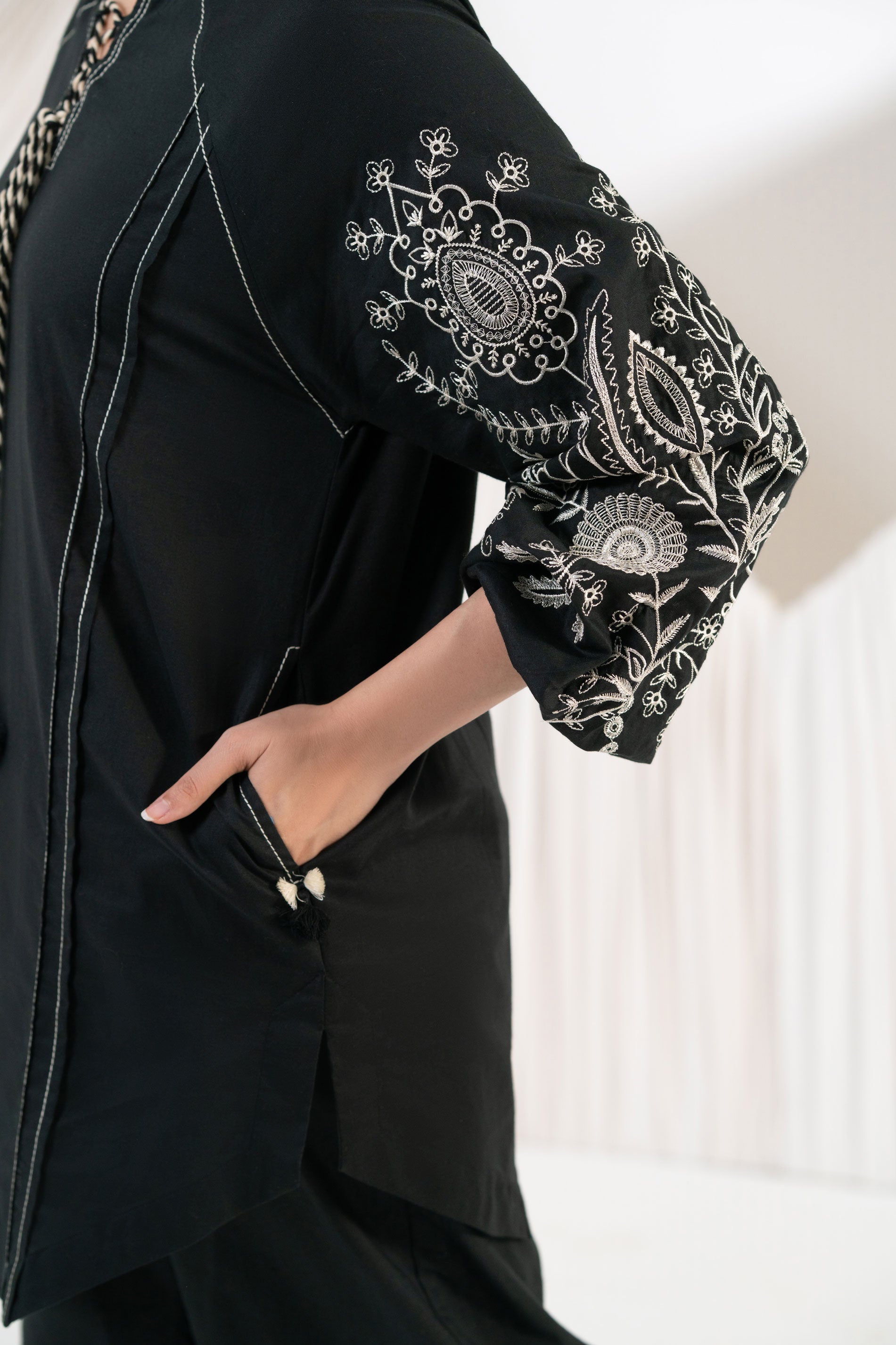 Black outfit with floral embroidery on sleeves against a white background