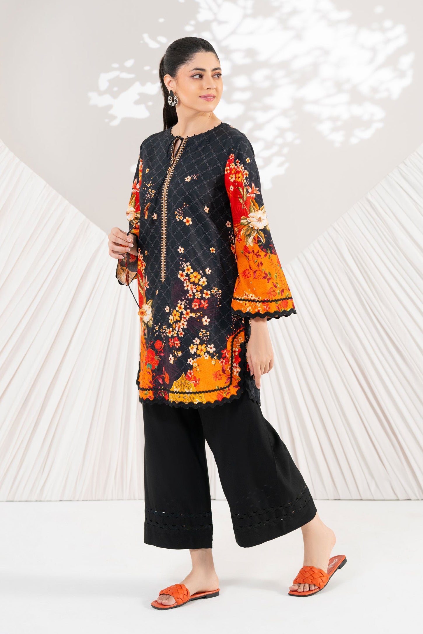Woman wearing a colorful embroidered outfit with black pants against a white background