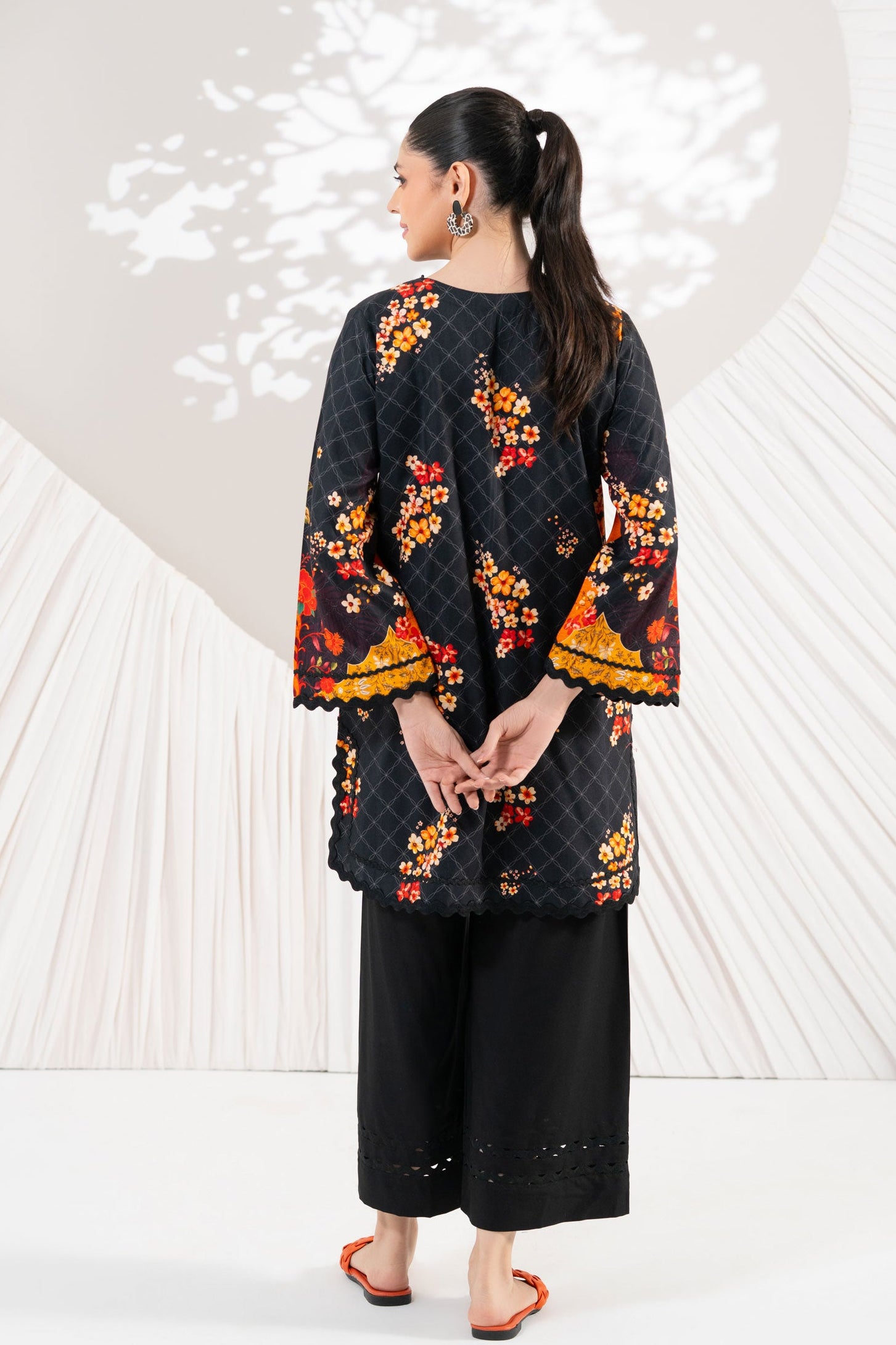 Woman wearing a black floral kimono-style top with wide-leg pants against a white background with heart shapes.