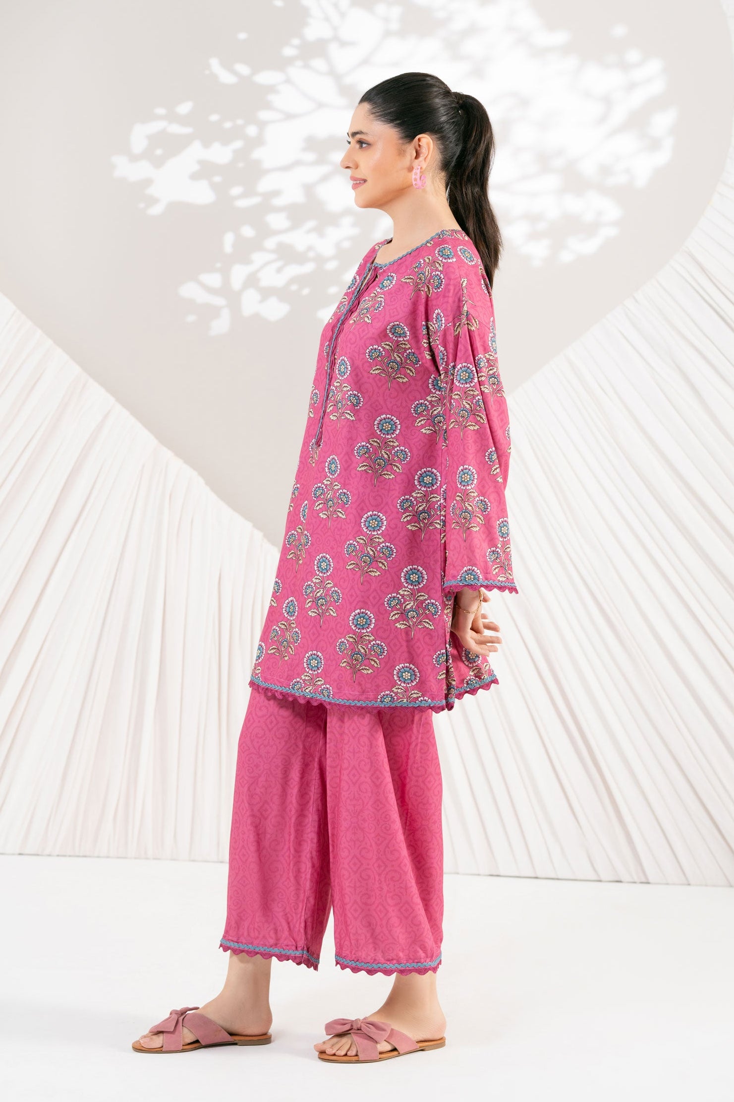 Woman wearing a pink traditional outfit with a floral pattern against a white background with heart shapes.