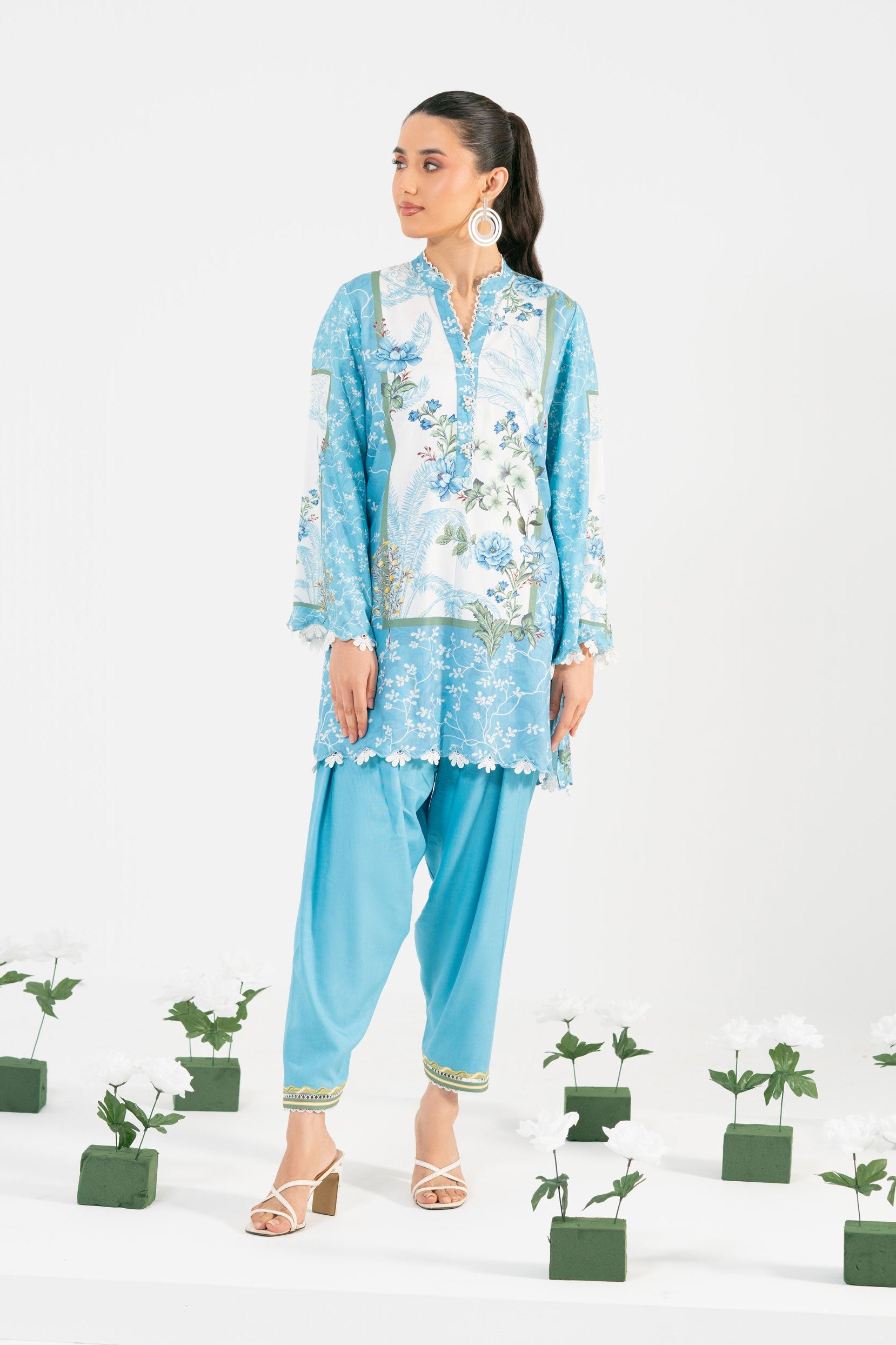 Woman in a blue traditional outfit standing among potted plants on a white background