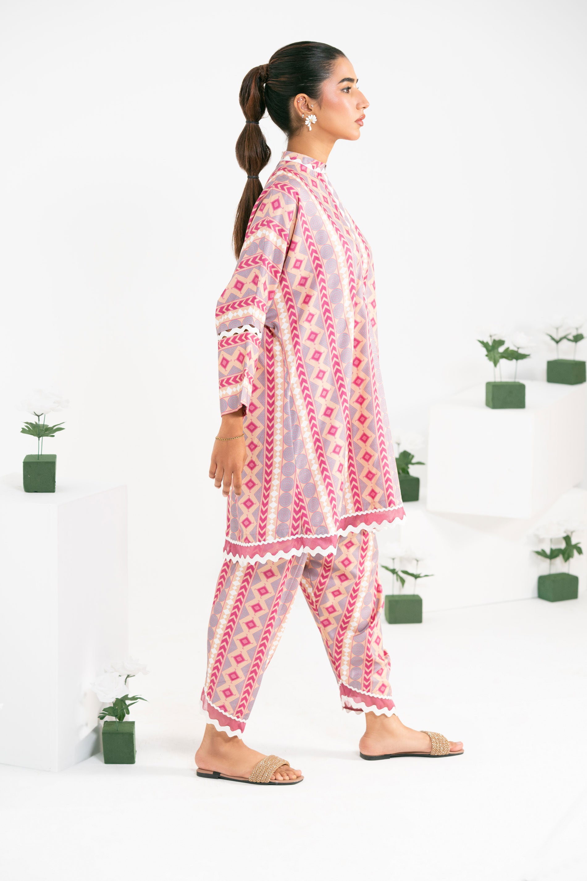 Woman wearing a pink and white patterned outfit with plants in the background