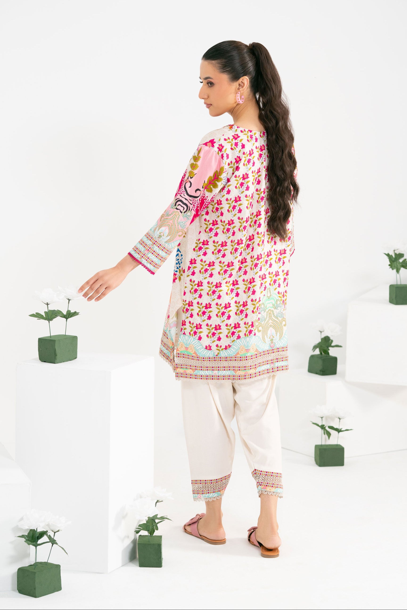 Woman wearing a floral top and white pants with plants in the background