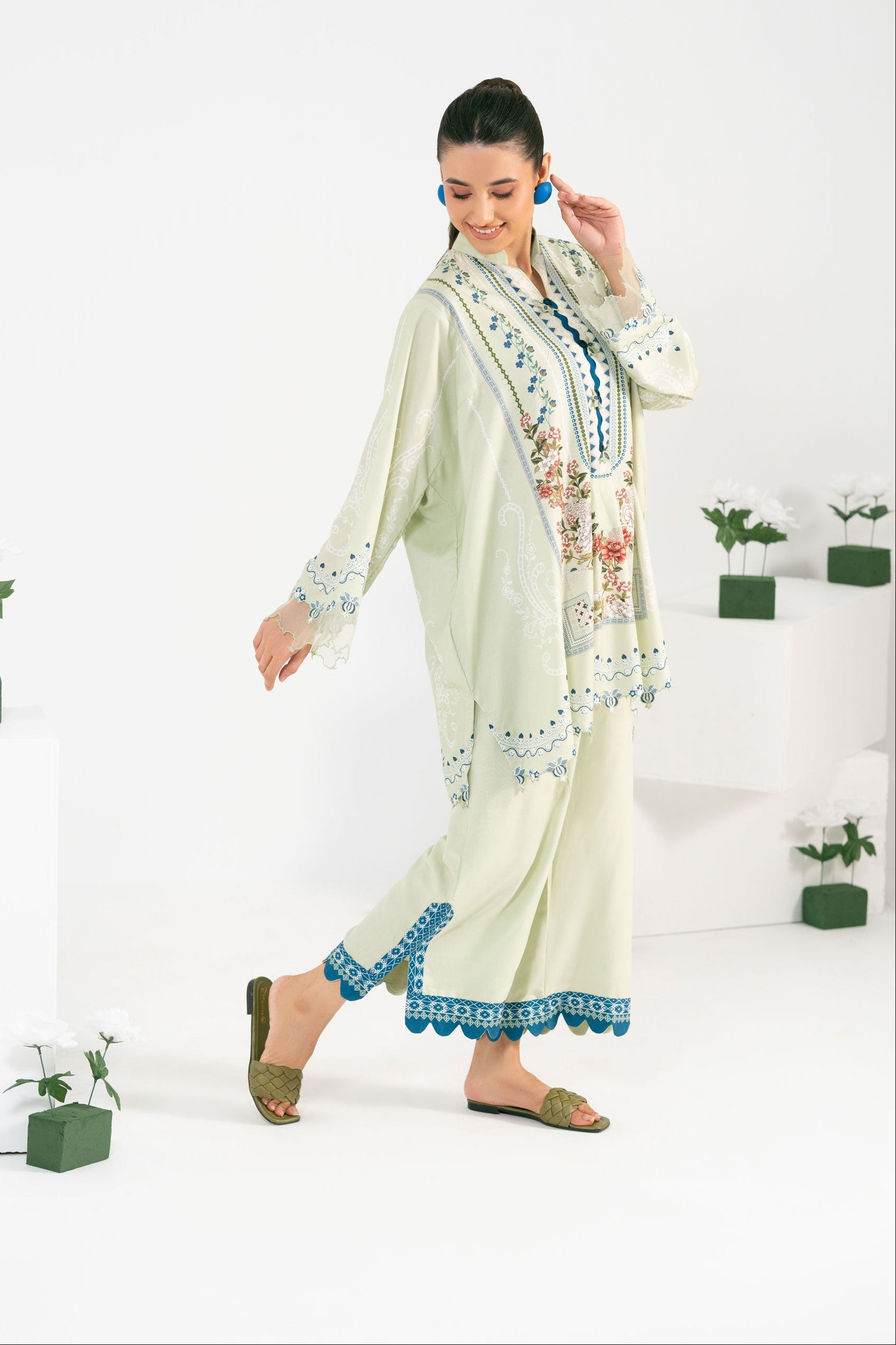 Woman wearing a light green traditional outfit with floral embroidery in a minimalistic setting.