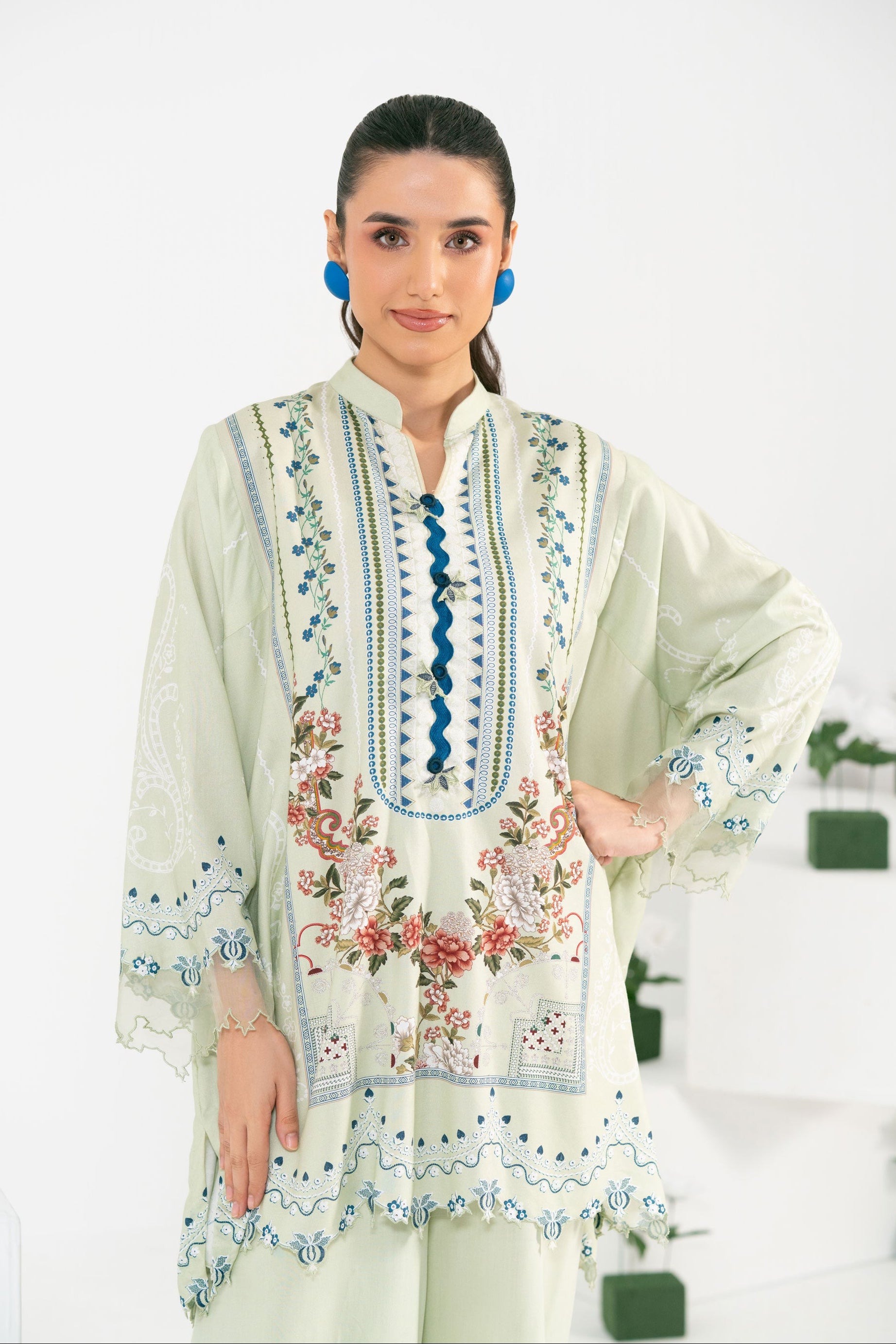 Woman wearing a light green embroidered dress with floral patterns on a white background
